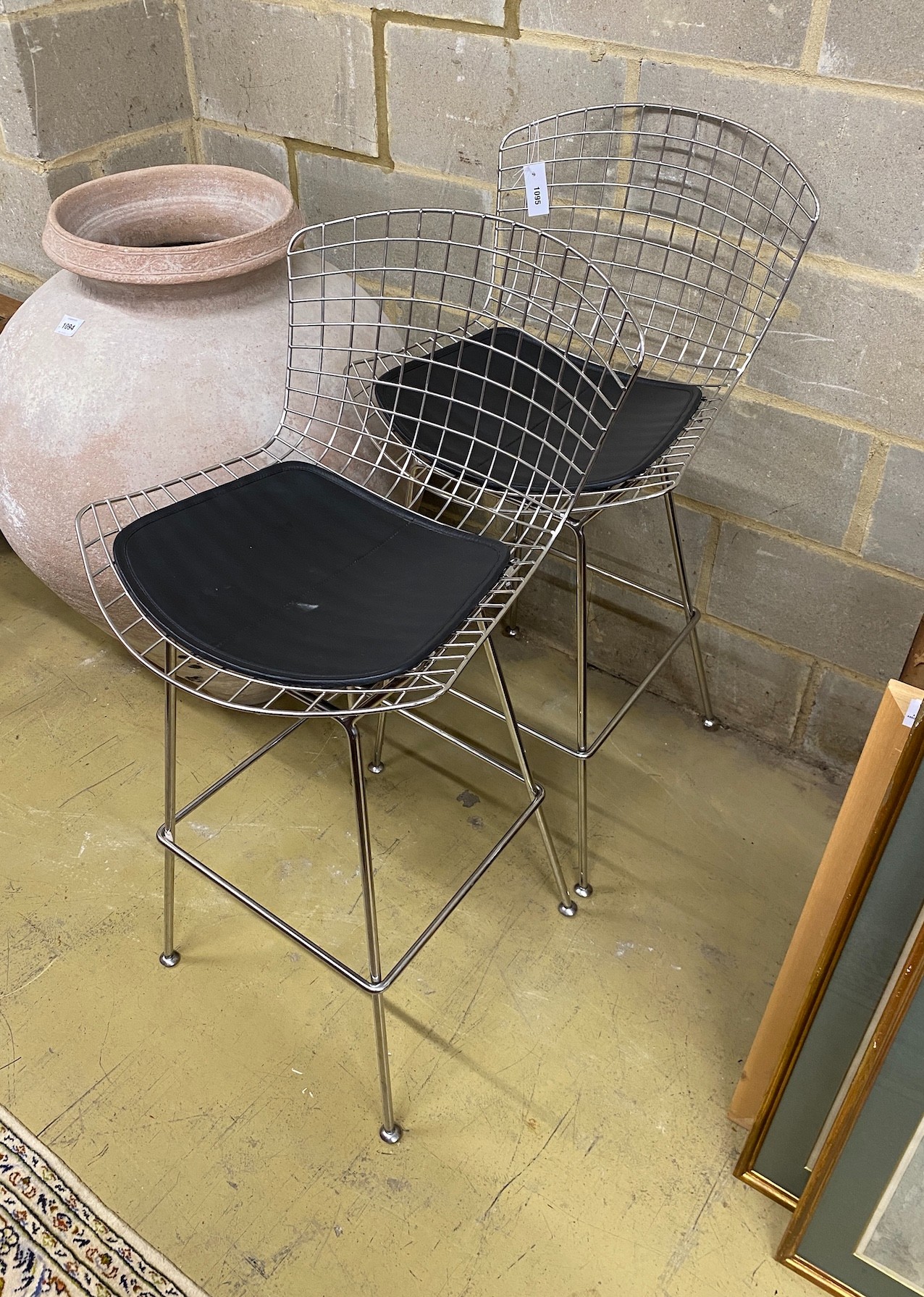 A pair of Harry Bertoia style chrome wired bar chairs with black leather seat pads, width 75cm, height 111cm